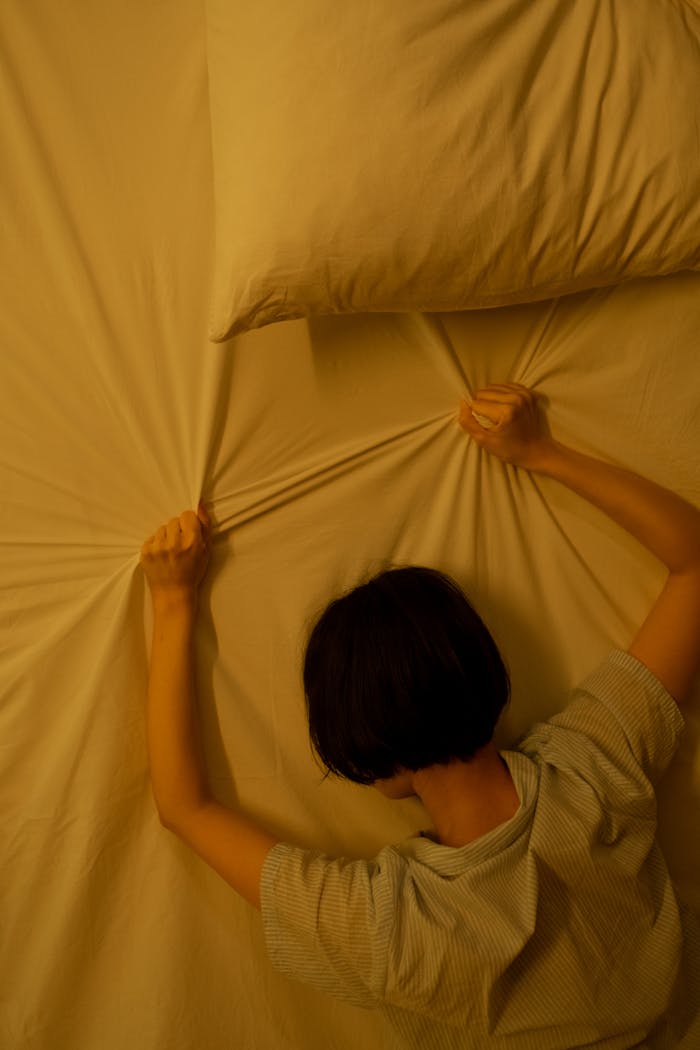 A woman on a bed gripping sheets in emotion, conveying stress or distress.
